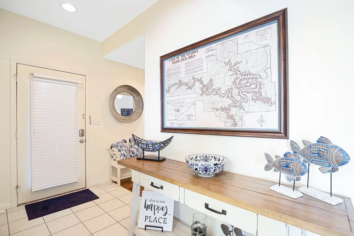A cheerful entryway scene featuring a map of the Ozarks, decorative fish sculptures, a ceramic bowl, and a wooden console table with a welcoming sign. The decor invites guests to explore the local area and hints at personalized local recommendations.