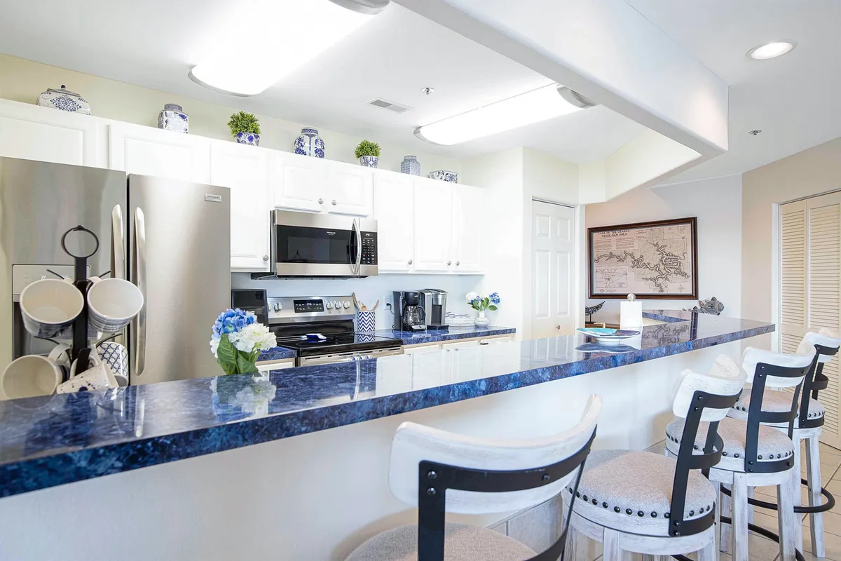 A bright kitchen scene featuring a blue granite countertop, crisp white cabinetry, kitchen appliances, and artfully arranged dishware. The ambience is cheerful and organized, evoking a sense of readiness for meal preparation and entertaining.