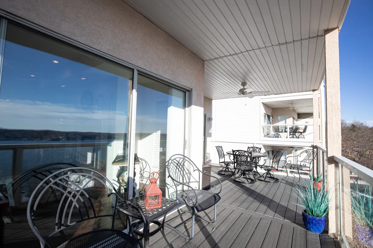 A peaceful patio is furnished with metal chairs, an outdoor table, lantern, and potted plants, all overlooking the water through glass doors. The setting is inviting for relaxing, entertaining, or soaking in lake views.