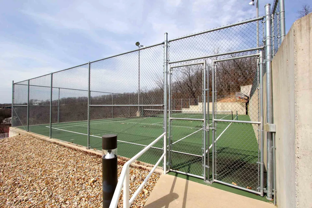 A bright, energetic exterior shot of the community pickleball (tennis) court, surrounded by a chain-link fence and natural landscape. The court is ready for play, inviting residents to engage in active, social matches with neighbors or friends.