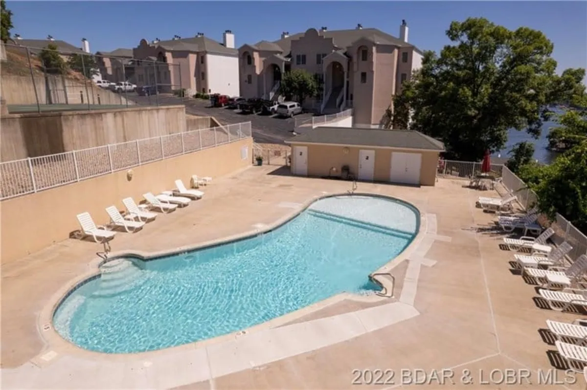 This exterior image centers on a sparkling community swimming pool surrounded by lounge chairs, neatly landscaped greenery, and portions of the surrounding condo buildings. The scene suggests a lively, family-friendly environment perfect for recreation and relaxation.