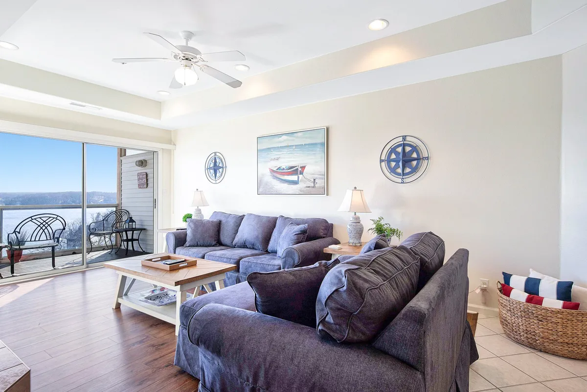 A comfortable living area featuring soft sofas, a central coffee table, and expansive windows that showcase beautiful water views. Nautical-themed wall art adds to the lakeside ambiance, creating a tranquil and social environment.