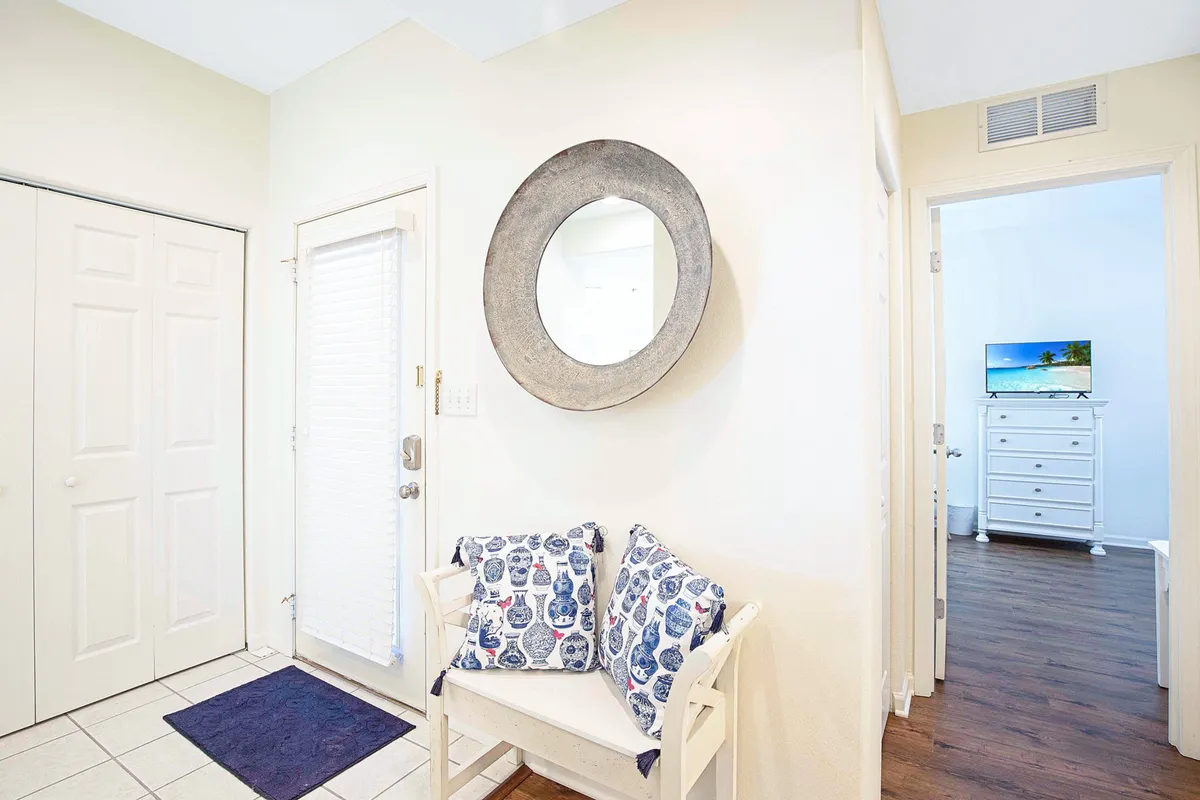 A welcoming entryway with a mirror, cushioned seating area, and a doorway leading further into the home. The space feels open and accessible, hinting at easy movement for guests of all ages.