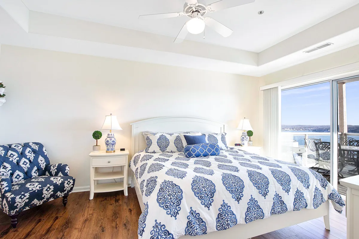A restful bedroom with patterned bedding, a blue accent chair, and sliding glass doors that open to a balcony. The room is designed for relaxation, with plenty of light and a calm, cozy décor.