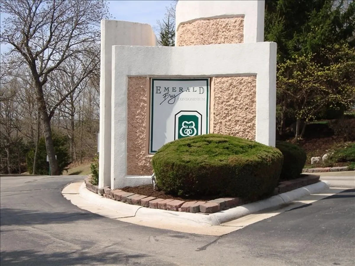 The entrance to the Emerald Bay community is shown, with its welcoming sign, manicured bushes, and landscaped details. The image gives a sense of arrival and hints at the broader neighborhood and outdoor opportunities nearby.